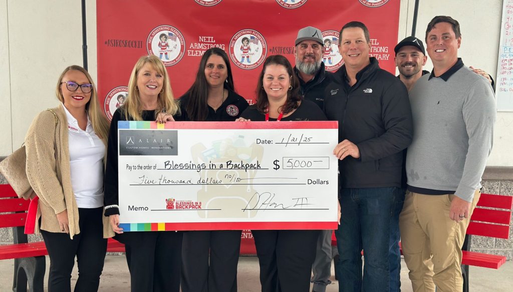 Alair Homes team members present a $5,000 check to Blessings in a Backpack and Neil Armstrong Elementary representatives during a donation ceremony. The team stands proudly with the check, showcasing their commitment to supporting children in need through the organization’s weekend food program.