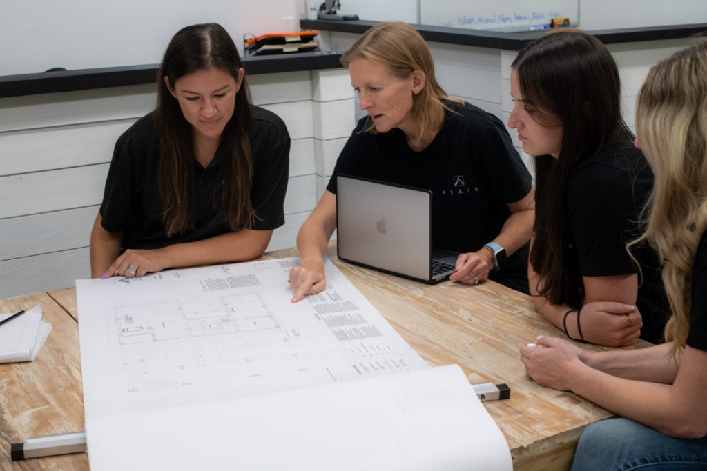 Four women collaborating over custom home plans, engaged in discussion about construction design and project details. Representing the next generation of industry leaders, they bring diverse perspectives to the future of homebuilding.