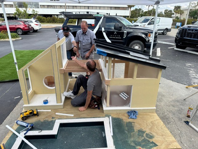 Alair Homes team constructing the walls and adding a metal roof to The Woof Lodge dog house.